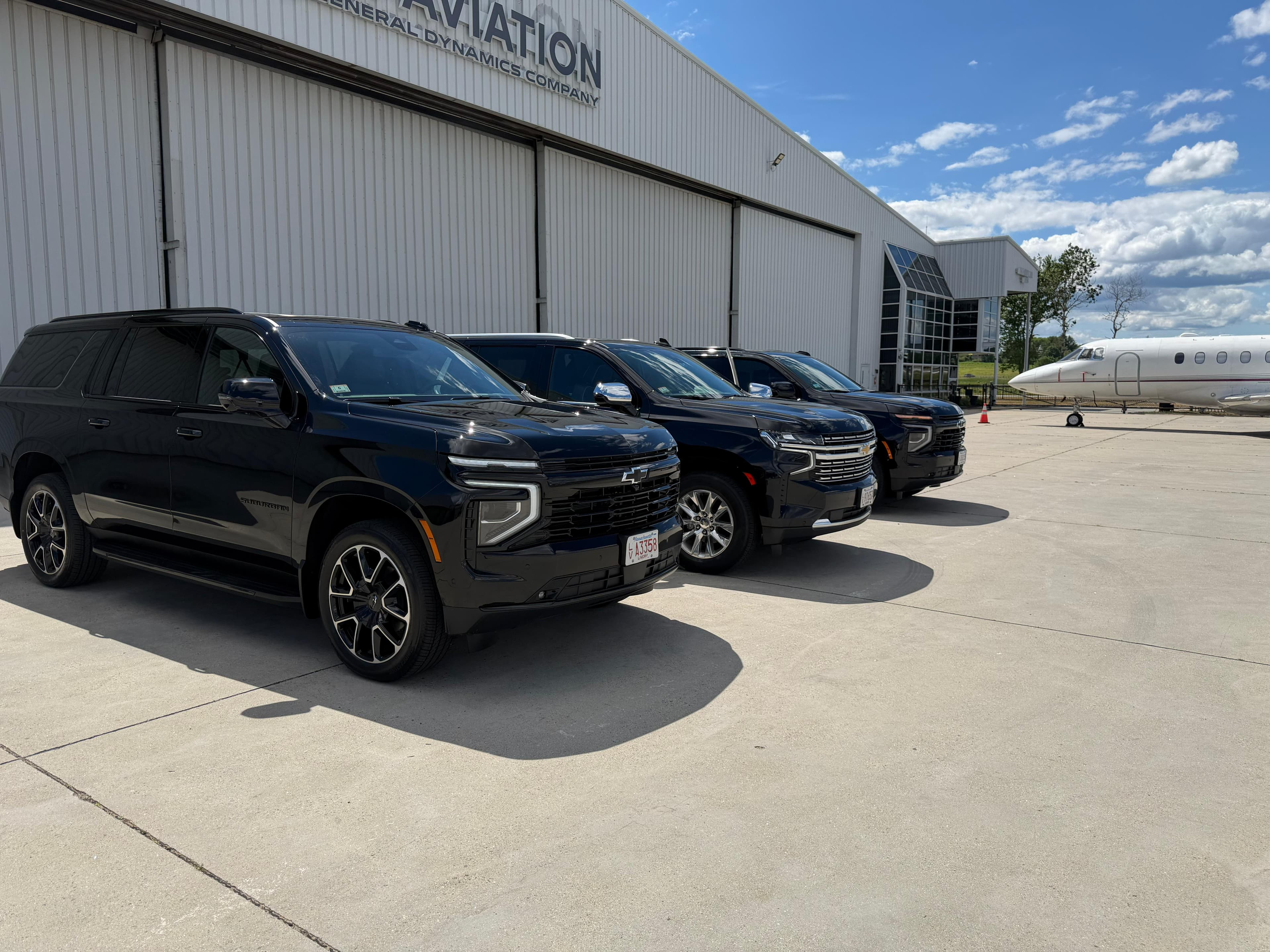 Three black Chevrolet Suburbans parked on an airport tarmac with a private jet nearby.