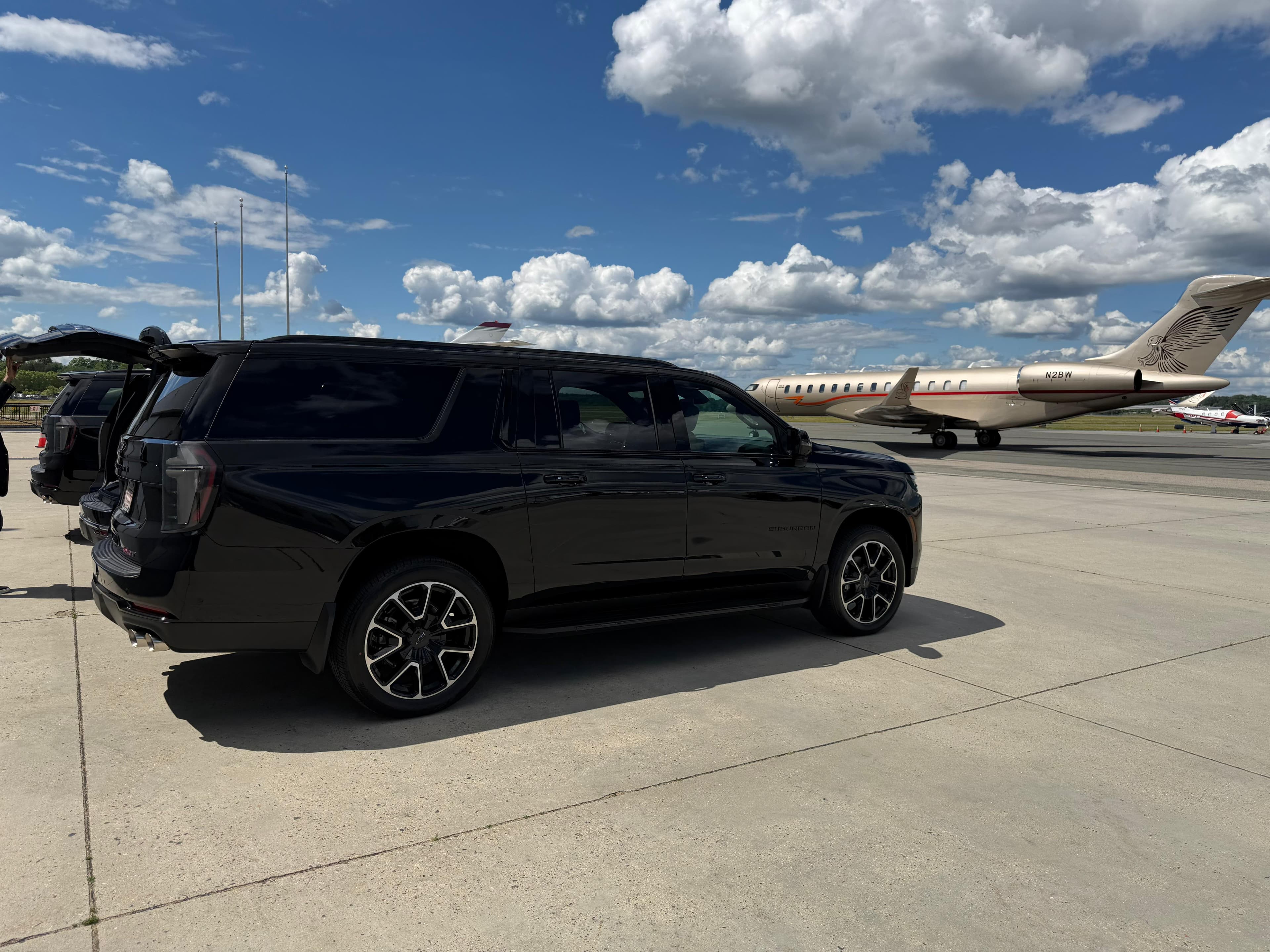 Black Chevrolet Suburban parked on an airport tarmac with a private jet in the background.